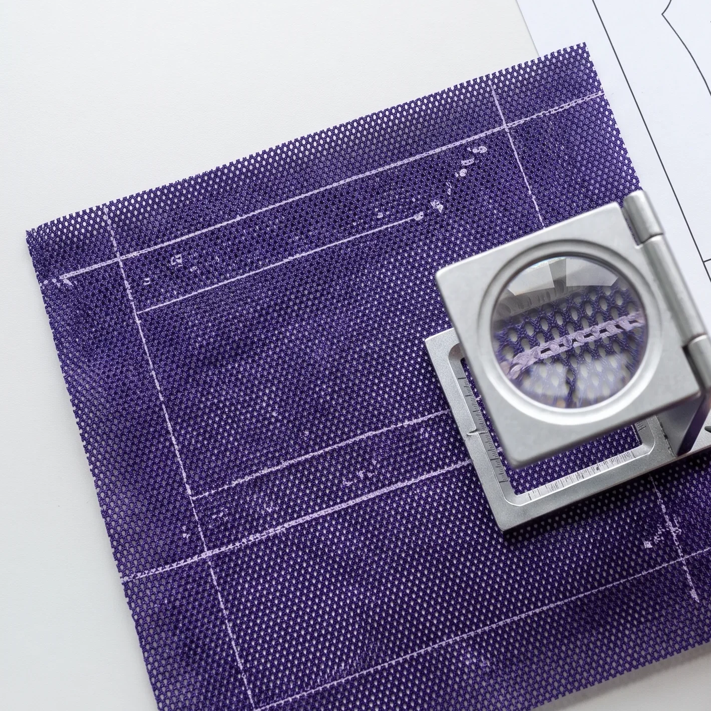A technician checking fine printed lines on a mesh strike-off through a linen tester loupe